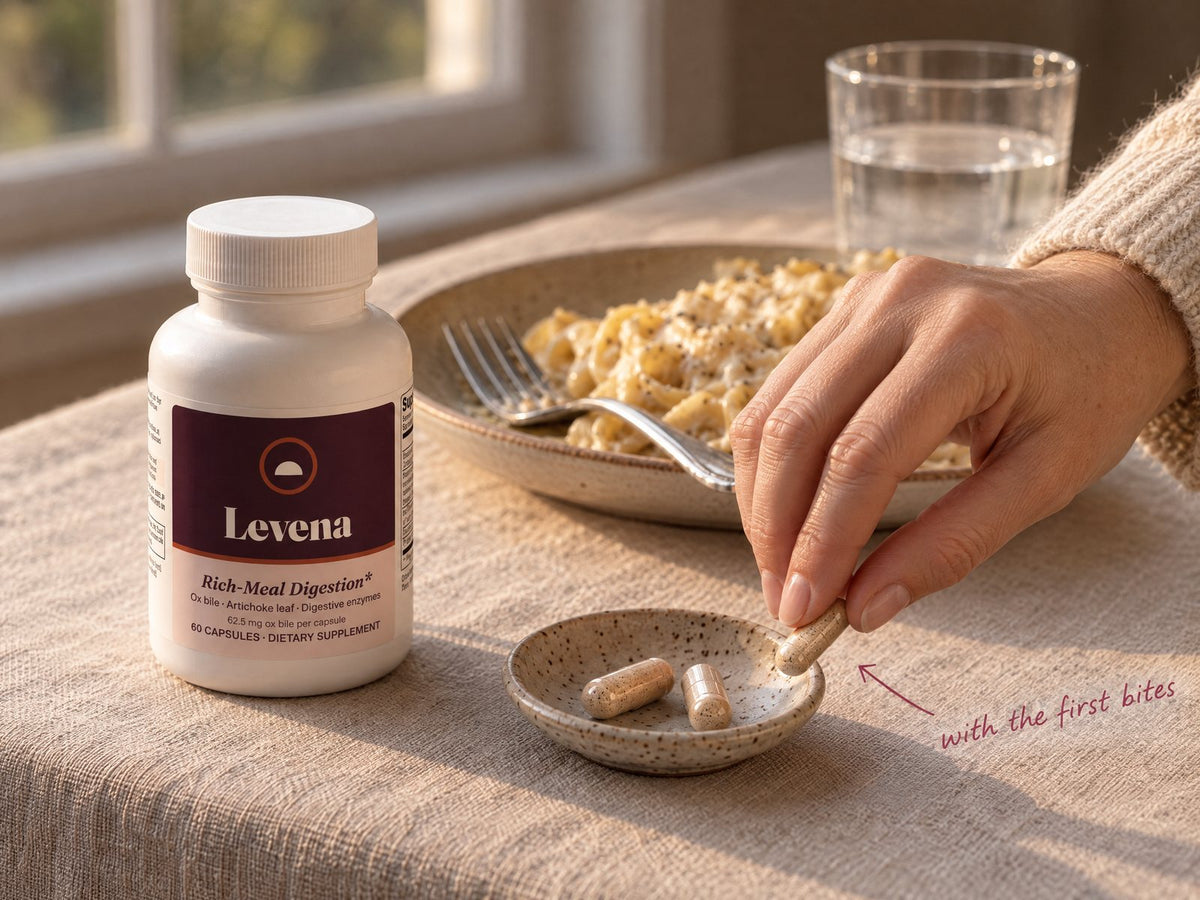A hand taking one Levena capsule at the start of a creamy pasta dinner